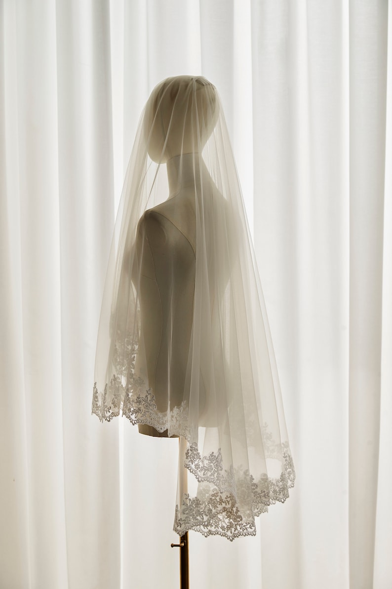May include: A white bridal veil with a delicate lace trim. The veil is made of soft tulle and is perfect for a wedding ceremony.