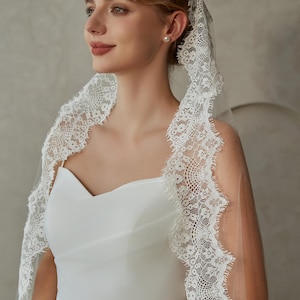 May include: A white bridal veil with a delicate lace trim. The veil is made of soft tulle and has a scalloped edge. The lace trim features a floral pattern.
