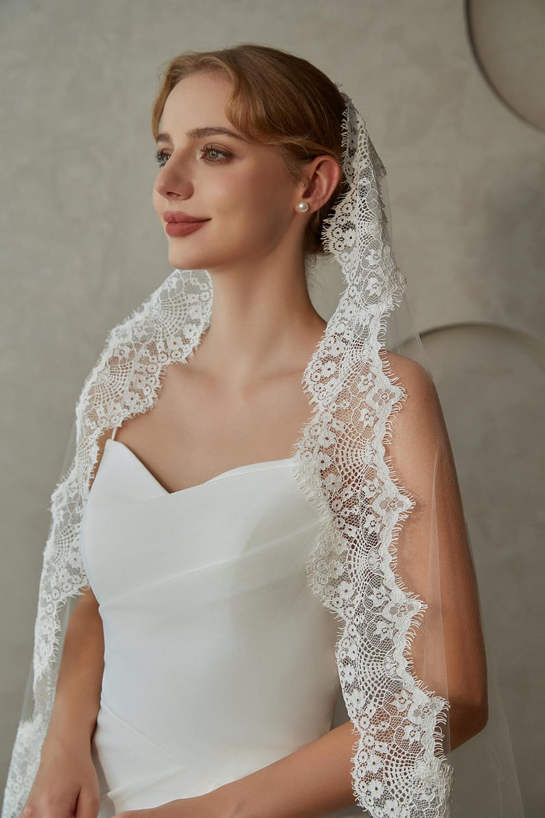 May include: A white bridal veil with a delicate lace trim. The veil is made of soft tulle and has a scalloped edge. The lace trim features a floral pattern.