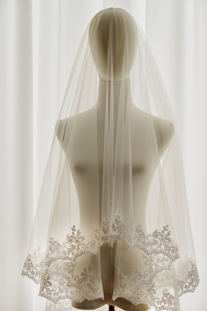 May include: A white bridal veil with a delicate lace trim. The veil is made of soft tulle and is perfect for a wedding ceremony.