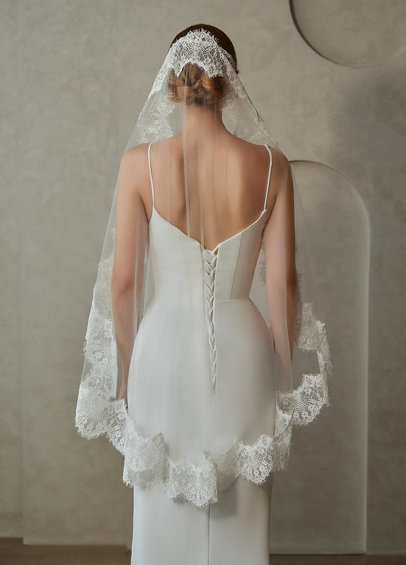 May include: A white bridal veil with a lace trim. The veil is made of soft tulle and has a delicate lace pattern. The veil is worn over a white dress.