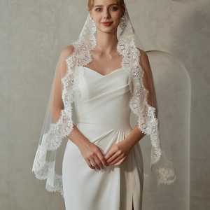 May include: A white bridal veil with a delicate lace trim. The veil is made of soft tulle and has a scalloped edge. The lace trim features a floral design.