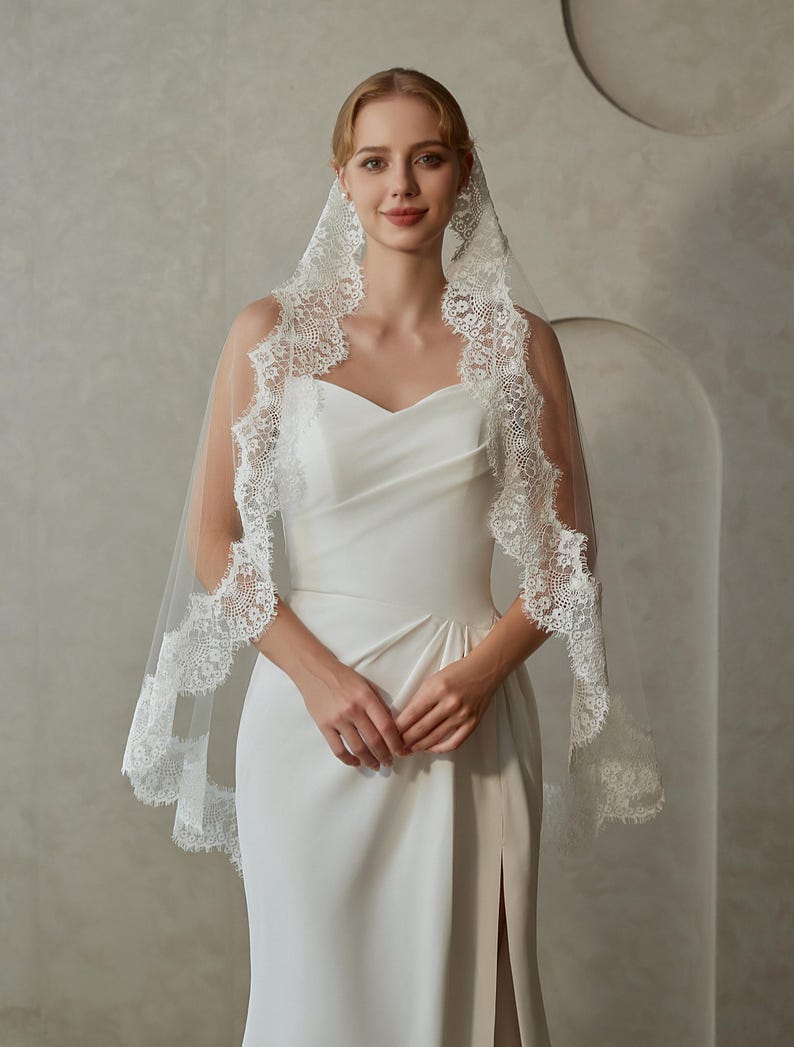 May include: A white bridal veil with a delicate lace trim. The veil is made of soft tulle and has a scalloped edge. The lace trim features a floral design.