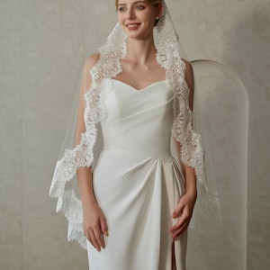 May include: A white bridal veil with a delicate lace trim. The veil is made of soft tulle and has a single layer. The lace trim is intricate and features a floral design.