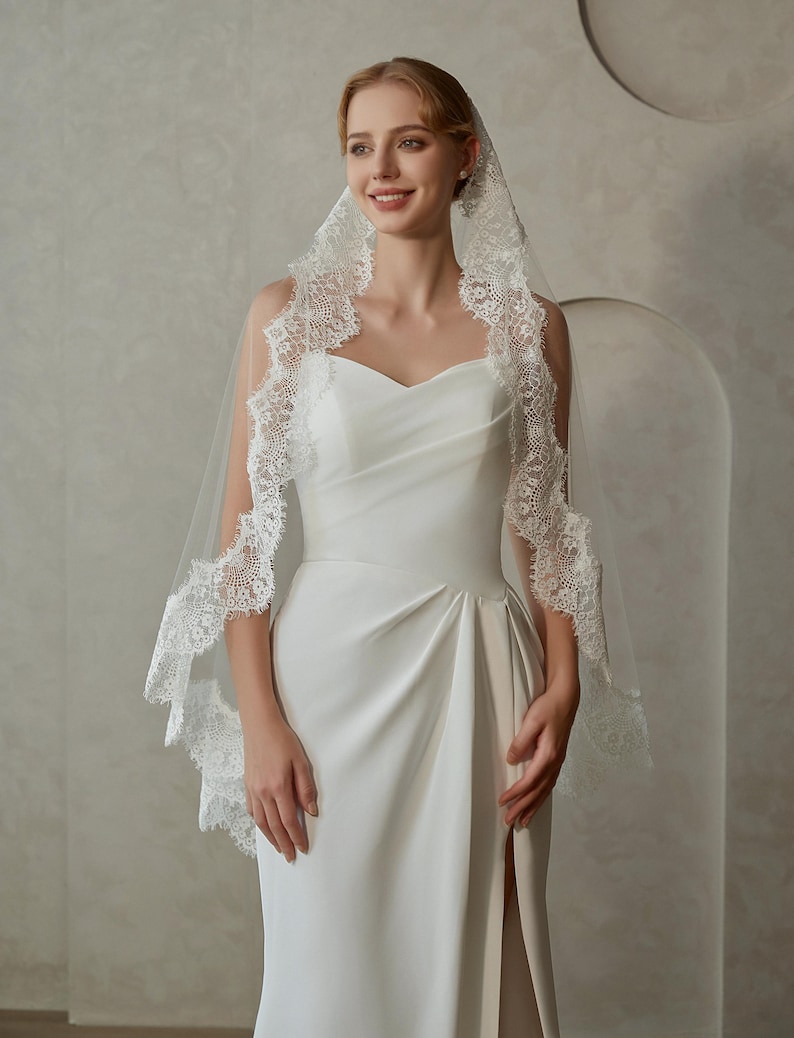 May include: A white bridal veil with a delicate lace trim. The veil is made of soft tulle and has a single layer. The lace trim is intricate and features a floral design.