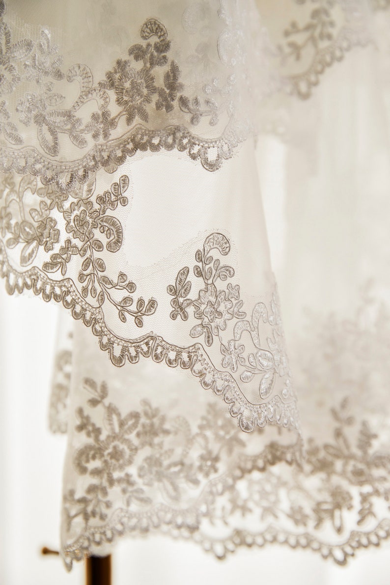 May include: White lace fabric with a delicate floral pattern. The lace is soft and flowing, with a subtle sheen.