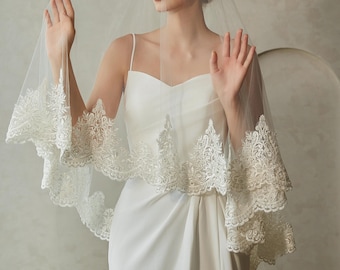 May include: A white bridal veil with a delicate lace trim. The veil is made of soft tulle and has a single layer. The lace trim is intricate and features a floral design.