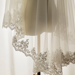 May include: A white bridal veil with a delicate lace trim. The veil is made of soft tulle and has a scalloped edge.