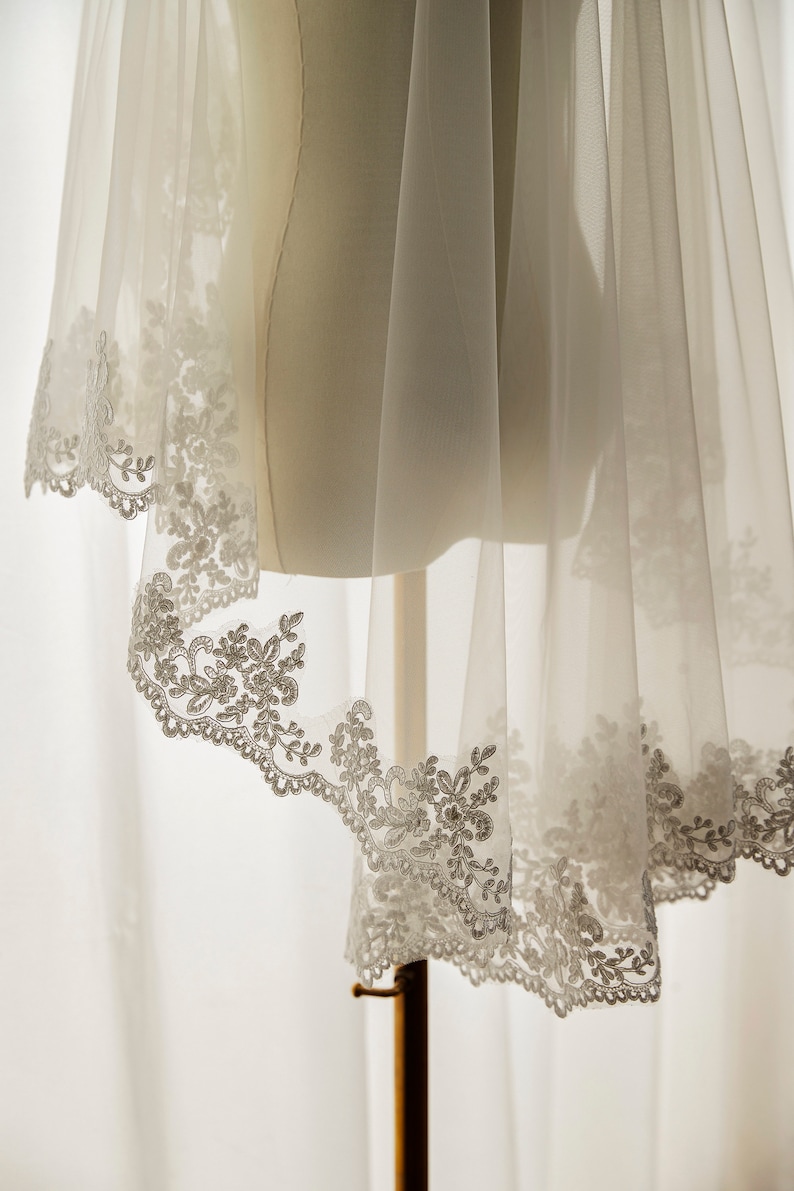 May include: A white bridal veil with a delicate lace trim. The veil is made of soft tulle and has a scalloped edge.