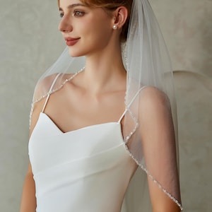 May include: A white bridal veil with a delicate beaded trim. The veil is made of soft tulle and is perfect for a simple and elegant wedding look.