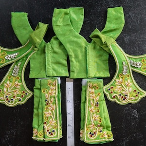 May include: Green fabric garment set with floral embroidery and sequins. The set includes two tops, two sleeves, and two skirts. The fabric is a soft, lightweight material. The embroidery is intricate and detailed. The sequins add a touch of sparkle.