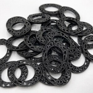 May include: A pile of black metal rings with intricate designs. The rings are all the same size and have a smooth, polished finish.