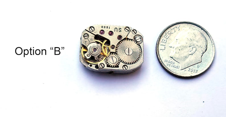 Peut inclure: Un petit mouvement de montre de couleur argent avec des engrenages dor&eacute;s et un rubis rouge. Le mouvement est &agrave; peu pr&egrave;s de la taille d'une pi&egrave;ce de dix cents.