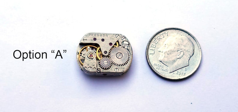 Peut inclure: Un petit mouvement de montre argent&eacute; avec des engrenages visibles et un rubis rouge. Le mouvement est &agrave; peu pr&egrave;s de la taille d'une pi&egrave;ce de dix cents.