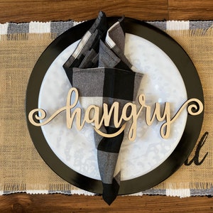 May include: A black and white checked napkin is folded and placed on a black and white marble plate. The plate is on a hessian placemat with black and white checked borders. A wooden sign with the word "hangry" is placed on the plate.