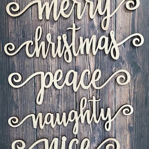 May include: Wooden cutout words spelling "merry christmas peace naughty nice" on a wood background.
