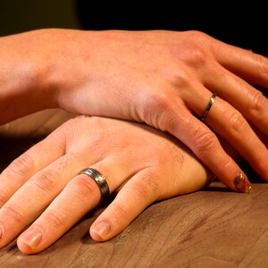 Two hands with Soilver wedding rings on a wooden surface