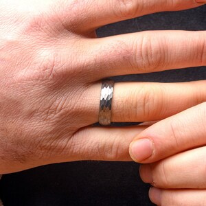 Hand wearing a silver ring with a textured band on a dark background