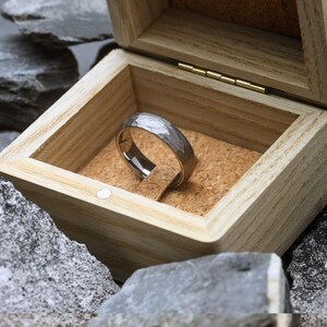 Silver ring in a wooden box with a natural stone background