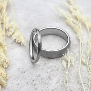Two silver rings on a textured surface with dried plants around