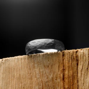 Silver ring with a textured surface on a wooden block against a black background