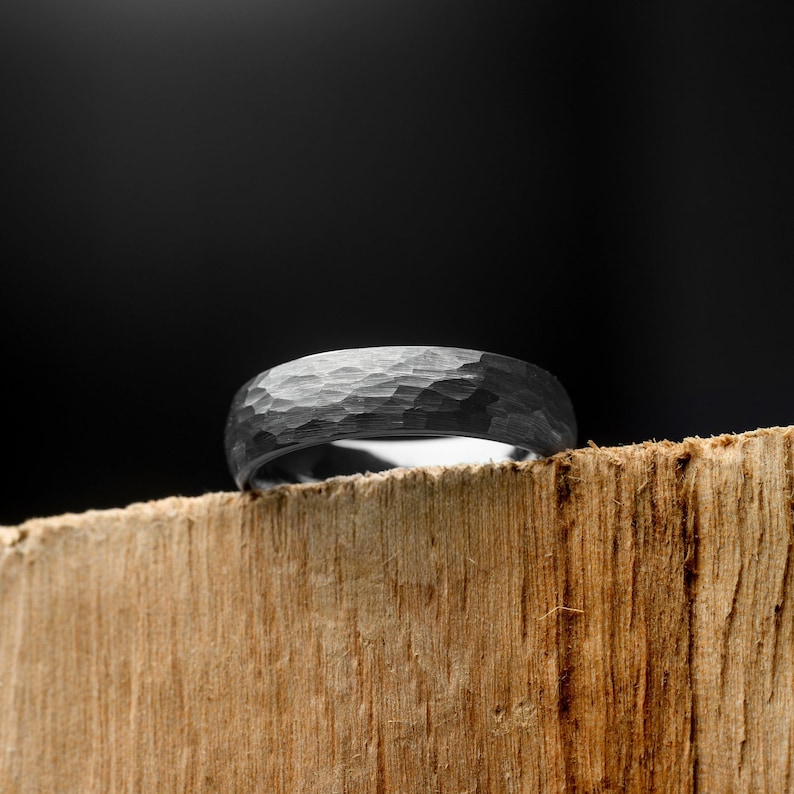 Silver ring with a textured surface on a wooden block against a black background