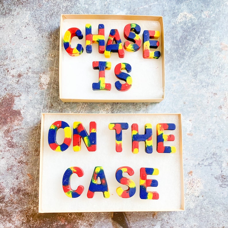 May include: Two boxes of colourful crayons spelling out "CHASE IS ON THE CASE". The crayons are in the shape of capital letters and are a mix of red, yellow, and blue colours. The crayons are in a cardboard box with white paper.