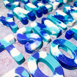 May include: A selection of resin letters and numbers in blue, teal, and white. The marbled effect gives a unique look. These decorative pieces are suitable for crafting or personalised gifts. Measurements are in centimetres.