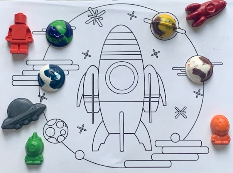 May include: A set of colorful wax crayons shaped like planets, a rocket ship, and a UFO. The crayons are on a white background with a black and white outline of a rocket ship and planets.