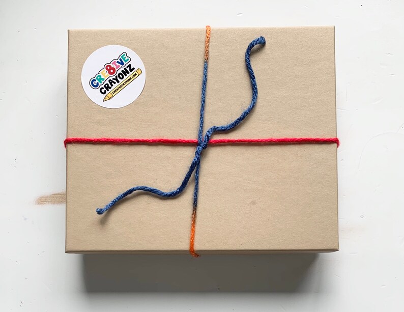 May include: A brown cardboard box tied with red and blue string. The box has a round sticker with the text "CRE8IVE CRAYONZ" on it.