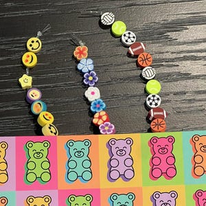 May include: A collection of colorful earrings featuring various designs. The earrings include smiley faces, flowers, and sports balls. A colorful pop art design of gummy bears in various colors is also visible.
