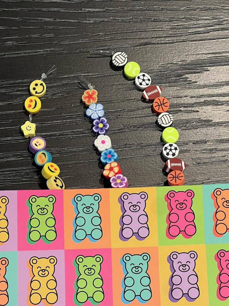 May include: A collection of colorful earrings featuring various designs. The earrings include smiley faces, flowers, and sports balls. A colorful pop art design of gummy bears in various colors is also visible.