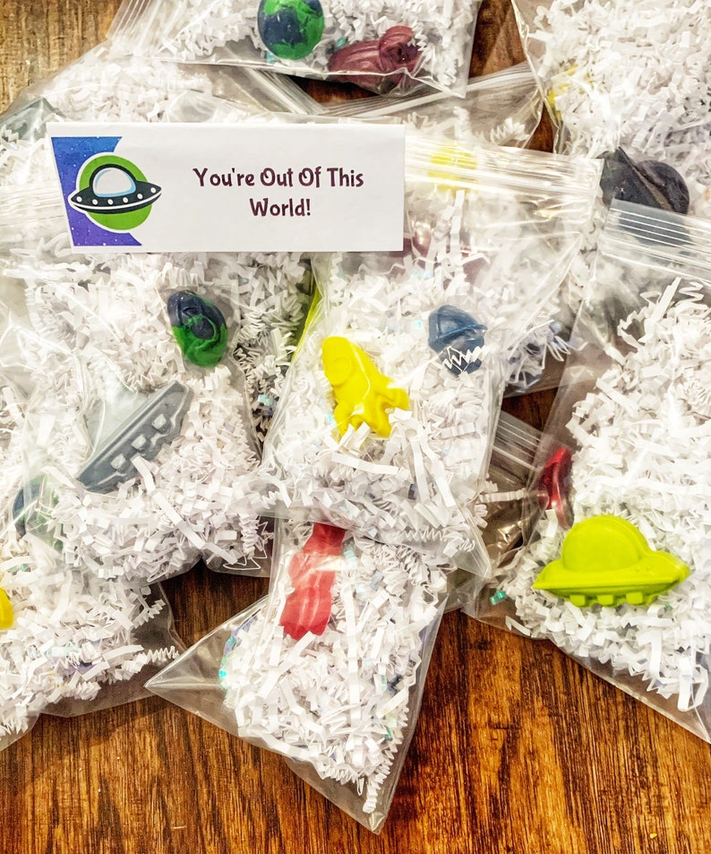 May include: A collection of small plastic bags filled with white shredded paper and colorful plastic toys. The bags have a tag that says "You're Out Of This World!" and a cartoon image of a UFO.