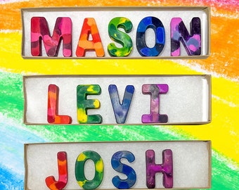May include: Three boxes with the names MASON, LEVI, and JOSH spelled out in colorful crayon letters. The letters are arranged in a row and are set against a rainbow background.