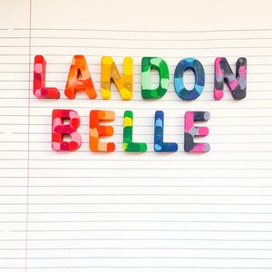 May include: Crayon letters spelling "LANDON BELLE" in a variety of colours, arranged on lined paper. The letters are in shades of red, orange, yellow, green, blue, and pink. Suitable for children's room decor or personalised gifts.