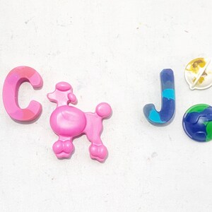 May include: Pink letter C, pink poodle figurine, blue letter J, and two small globe-shaped figurines, one with a yellow and brown design and the other with a green and blue design, on a white background.