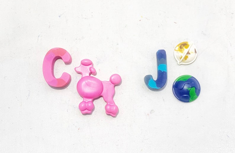 May include: Pink letter C, pink poodle figurine, blue letter J, and two small globe-shaped figurines, one with a yellow and brown design and the other with a green and blue design, on a white background.