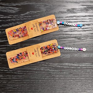 May include: Two handmade resin bookmarks with colorful confetti and the text "Handmade with love." One bookmark has a beaded charm that spells "DAISY," and the other says "PALMER."