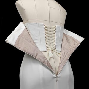 May include: A white corset with a white lace-up back. The corset is open in the front, revealing a white lining.