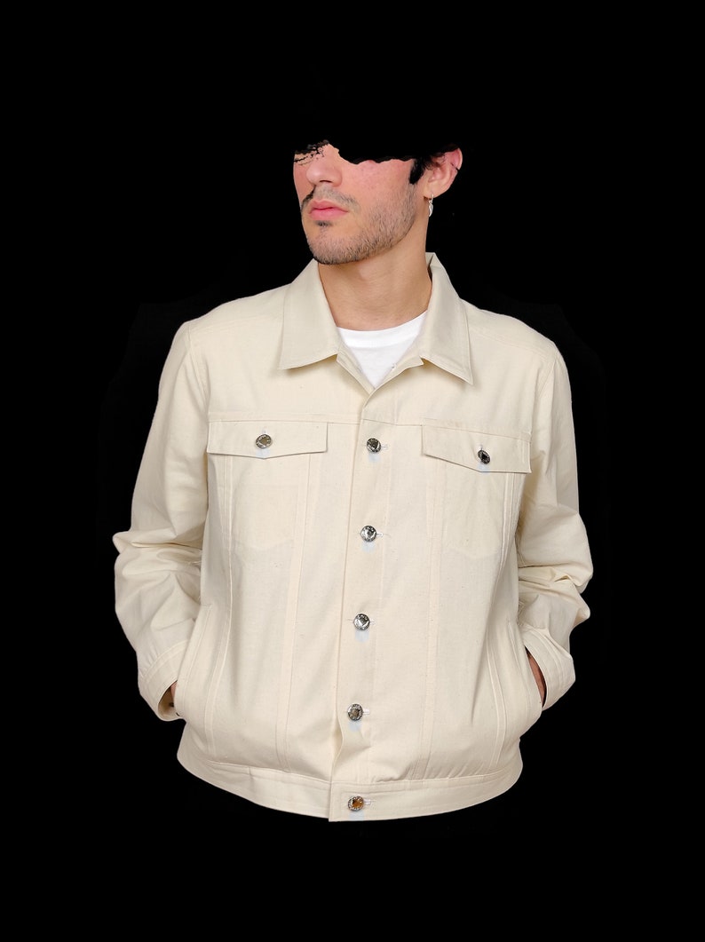 May include: A cream colored denim jacket with a button front closure and two chest pockets.