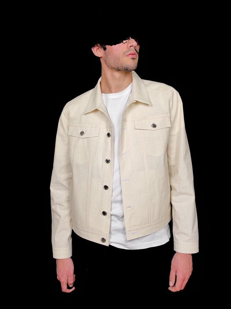 May include: A cream-colored denim jacket with a button-up front and two flap pockets. The jacket has a classic fit and is made of a soft, comfortable fabric.