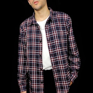 May include: A long-sleeved plaid shirt in shades of red, white, and blue. The shirt has a button-down collar and a chest pocket.