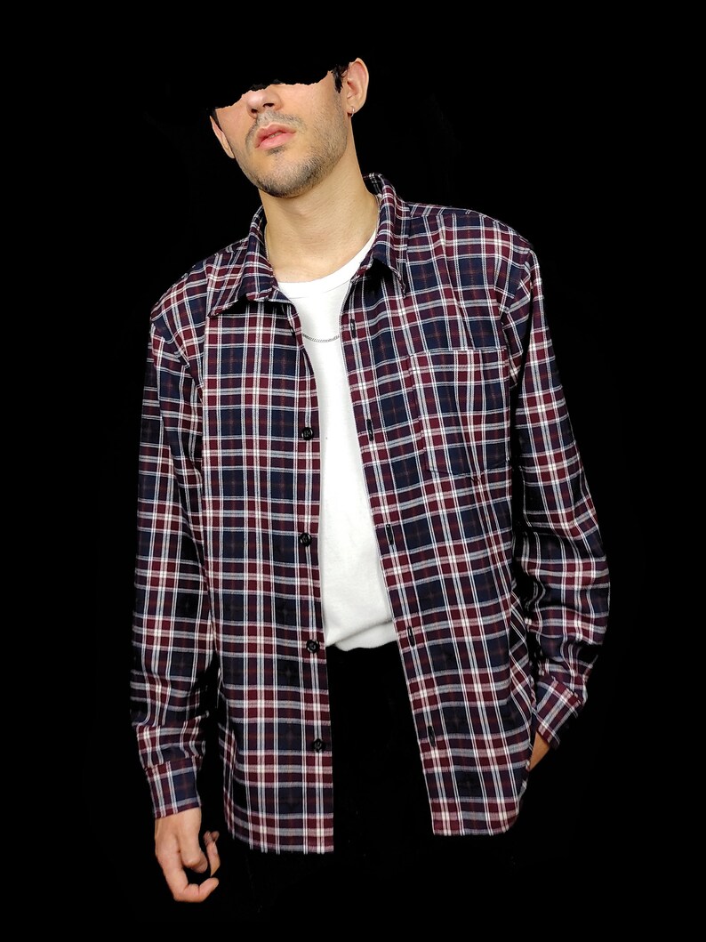 May include: A long-sleeved plaid shirt in shades of red, white, and blue. The shirt has a button-down collar and a chest pocket.