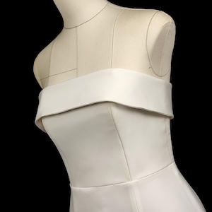 May include: A white strapless dress with a fitted bodice and a flowing skirt. The dress is made of a smooth, satin-like fabric.