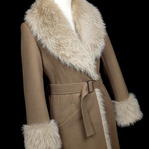 May include: A tan-colored coat with a faux fur collar and cuffs. The coat features a belt with a rectangular buckle and a tailored silhouette. The faux fur trim is a light beige color, and the coat has a classic, elegant design.