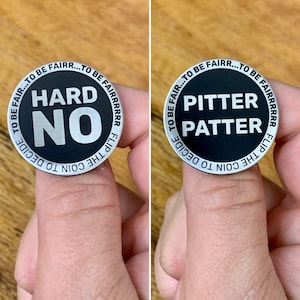 May include: A black and silver coin with the words "HARD NO" on one side and "PITTER PATTER" on the other. The coin's edge reads "TO BE FAIR...TO BE FAIRR...TO BE FAIRRRRR FLIP THE COIN TO DECIDE".