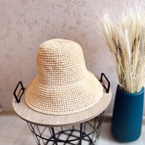 May include: A light brown woven straw bucket hat with a wide brim, sitting on a wooden top of a black wire basket.