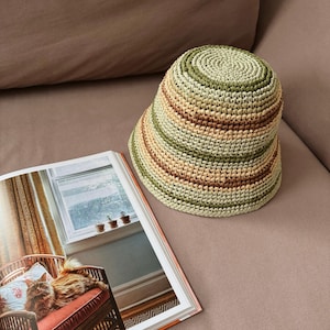 May include: A green, brown, and beige striped crocheted bucket hat. The hat is made of a woven straw material.