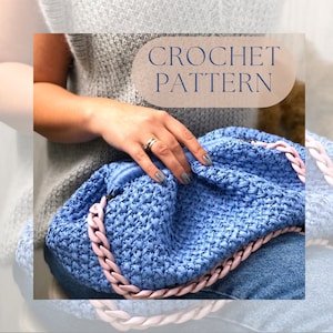 May include: A light blue crochet bag with a pink chain strap. The bag is made with a textured stitch and has a slouchy, casual look. CROCHET PATTERN is written in a circle on the image.
