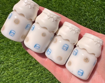 Puede incluir: Cuatro mini botellas de leche blancas con diseños de galletas azules y marrones y tapas blancas con un lazo en la parte superior.